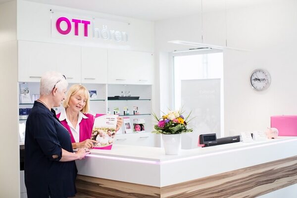 Hörakustikerin berät Kundin im modernen Hörakustik-Fachgeschäft OTT hören am Empfang.