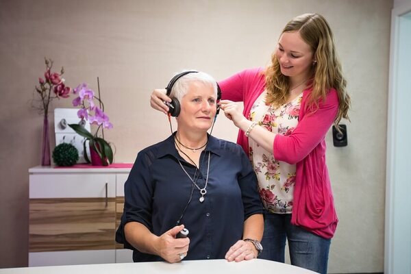 Eine Hörakustikerin führt bei einer älteren Frau einen Hörtest mit Kopfhörern durch.